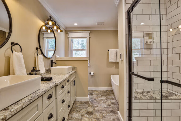 Spacious master bathroom at The Farmhouse in Ellijay, GA, with double vanity, framed mirrors, and walk-in shower with bench.